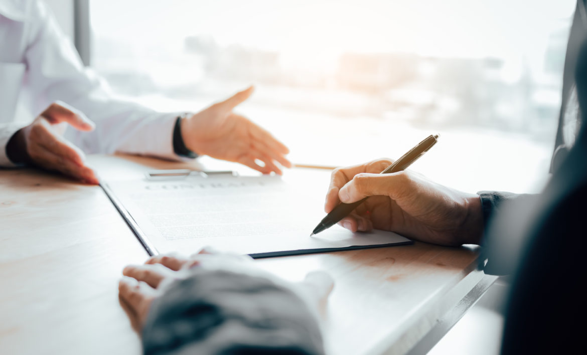 Client signing a real estate contract on desk in office.